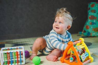 7 aylık küçük bir çocuk dik oturmayı öğreniyor. Bir bebek yerde otururken oyuncaklarla oynar. Bebekler için eğitici oyuncaklar.