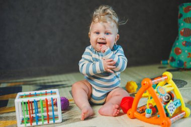 7 aylık küçük bir çocuk dik oturmayı öğreniyor. Bir bebek yerde otururken oyuncaklarla oynar. Bebekler için eğitici oyuncaklar.