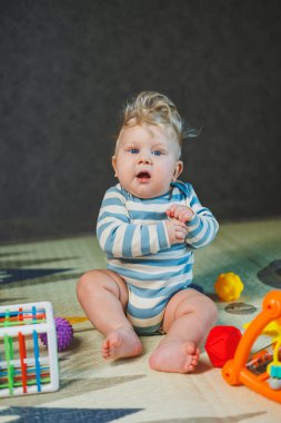 7 aylık küçük bir çocuk dik oturmayı öğreniyor. Bir bebek yerde otururken oyuncaklarla oynar. Bebekler için eğitici oyuncaklar.