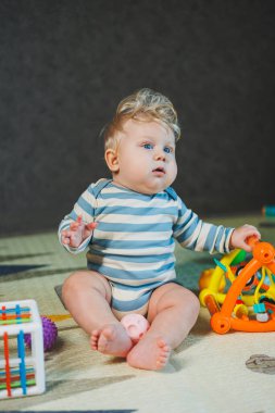 7 aylık bir çocuğun yerde oturup oyuncaklarla oynadığı fotoğraf. Çocuk gülümsüyor ve oyuncaklarla oynuyor..