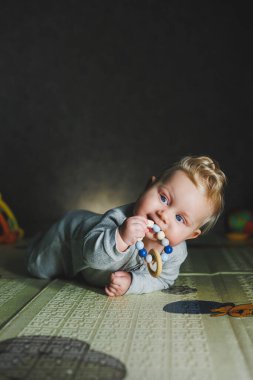 8 aylık bir çocuk yerde yatıyor ve bir ipin ucunu kemiriyor. Bebek oyuncaklarla oynar