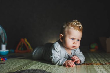 8 aylık bir çocuk yerde yatıyor ve bir ipin ucunu kemiriyor. Bebek oyuncaklarla oynar
