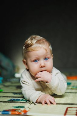 Evde 7-9 aylık bir bebeğin fotoğrafı. Gülümseyen bir çocuk yerde yatar ve oyuncaklarla oynar. Yerde oturan tatlı çocuk..