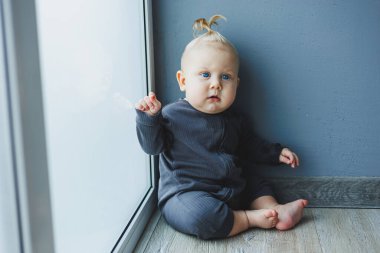 Kafasında kuyruğu olan 7 aylık küçük bir çocuk. Bebek yerde oturuyor ve gülümsüyor..