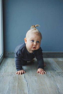 Bebek yürümeyi öğreniyor. Kafasında kuyruğu olan 7 aylık küçük bir çocuk. Bebek yerde oturuyor ve gülümsüyor..