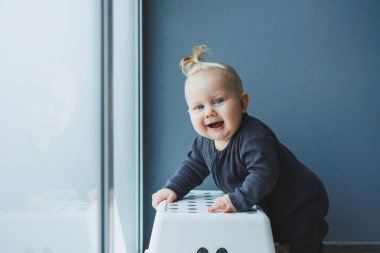 Evin içinde 7-9 aylık bir çocuğun fotoğrafı. Meraklı, gülümseyen bir çocuk etrafındaki dünyayı keşfediyor. Sandalyenin yanında duran sevimli bebek. Çocuk ayağa kalkıp yürümeyi öğreniyor..