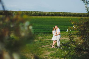 Sevecen, romantik, hamile bir çift çiçek açan elma bahçesinde sarılıyor. Beyaz çiçek açan ağaçların parkında beklenen ebeveynler. Bir çift bebek bekliyor.