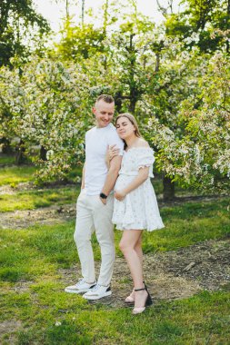 Bahar bahçesinde güzel genç bir çift. Güzellik yaşam tarzı aile kavramı. Mutlu bir anne bebek bekliyor. Çiçek açan bahçede mutlu genç bir çift.