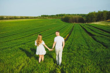Yeşil bir bahar tarlasında sarılan hamile bir çift. Beyaz çiçek açan ağaçların parkında beklenen ebeveynler. Bebek bekleyen romantik bir çift. Yeşil bir tarlada yürüyüş