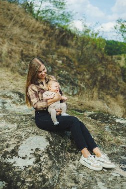 Genç bir anne parkta dururken küçük oğlunu kollarında tutuyor. Bir anne oğluyla oynuyor..