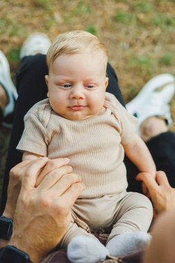 Annesinin kollarında, 2 aylık bir çocuğun yakın plan fotoğrafı var. Bebek annesinin kollarında yatarken gülümsüyor..