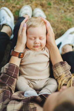 Annesinin kollarında, 2 aylık bir çocuğun yakın plan fotoğrafı var. Bebek annesinin kollarında yatarken gülümsüyor..