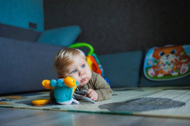 Çocuk renkli oyuncak bloklarıyla oynuyor. Çocuklar oynar. Küçük çocuk güneşli beyaz yatak odasındaki karanlık zeminde oyuncaklardan kule inşa ediyor. Bebek ve bebek için eğitici bir oyun. Çocuklar oyuncak ev yapar.