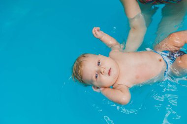 2 yaşındaki küçük bir çocuk bir koçla havuzda yüzmeyi öğreniyor. Çocuklar için yüzme dersleri