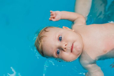 2 yaşındaki küçük bir çocuk bir koçla havuzda yüzmeyi öğreniyor. Çocuklar için yüzme dersleri