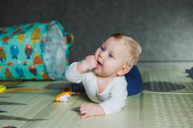 Dört aylık bir çocuk halıya uzanıyor ve oyuncaklarla oynuyor. Çocuk başını tutuyor. Bir bebek yerde sürünmeyi öğrenir.