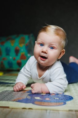 Dört aylık bir çocuk halıya uzanıyor ve oyuncaklarla oynuyor. Çocuk başını tutuyor. Bir bebek yerde sürünmeyi öğrenir.