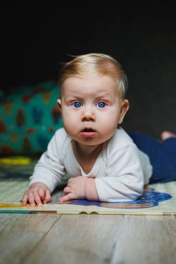 Dört aylık bir çocuk halıya uzanıyor ve oyuncaklarla oynuyor. Çocuk başını tutuyor. Bir bebek yerde sürünmeyi öğrenir.