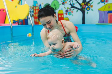 Bir bebek havuzda koçla yüzmeyi öğrenir. Bebekler için yüzme havuzu.