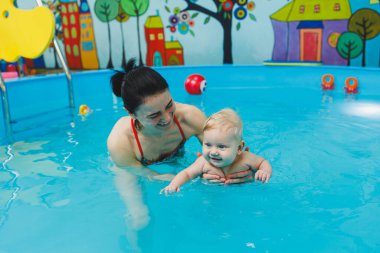 Bir bebek havuzda koçla yüzmeyi öğrenir. Bebekler için yüzme havuzu.