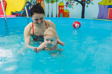 Bir bebek havuzda koçla yüzmeyi öğrenir. Bebekler için yüzme havuzu.