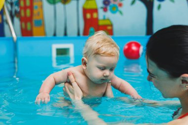 Bir bebek havuzda koçla yüzmeyi öğrenir. Bebekler için yüzme havuzu.