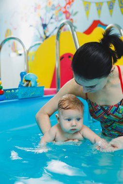 2 yaşındaki küçük bir çocuk bir koçla havuzda yüzmeyi öğreniyor. Çocuklar için yüzme dersleri