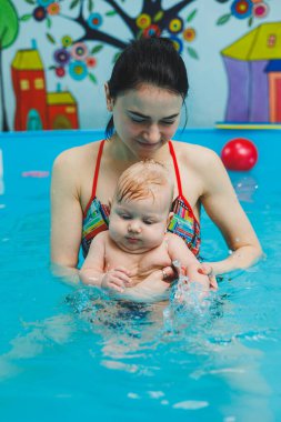 2 yaşındaki küçük bir çocuk bir koçla havuzda yüzmeyi öğreniyor. Çocuklar için yüzme dersleri