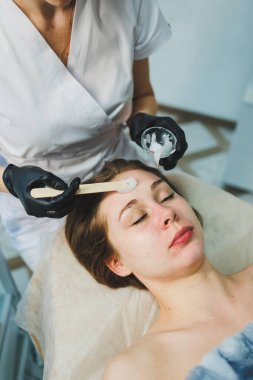 Güzellik salonundaki bir kadının yüzüne maske takan bir güzellik uzmanının elleri. Estetik prosedür. Yüz bakımı.