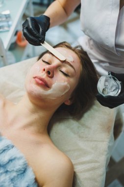 Güzellik salonundaki bir kadının yüzüne maske takan bir güzellik uzmanının elleri. Estetik prosedür. Yüz bakımı.