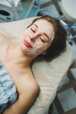 Beyaz krem maskeli bir kadın yüzü. Kişisel cilt bakımı. Yüze nemlendirici soyulan maske. Tıp ve kozmetoloji.