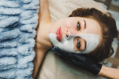 Güzellik salonundaki bir kadının yüzüne maske takan bir güzellik uzmanının elleri. Estetik prosedür. Yüz bakımı.