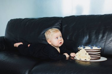 10 aylık bir erkek bebek lezzetli bir pastanın yanında yatıyor. Küçük bir çocuk için bir pasta..