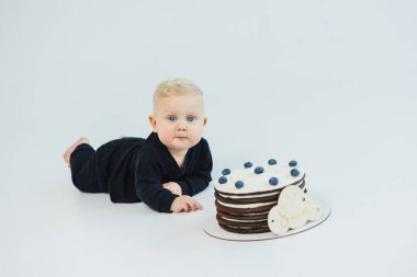 8 aylık beyaz bir geçmişi olan küçük bir çocuk bir pastanın yanında yatıyor. Küçük bir çocuk için tatlı pasta..