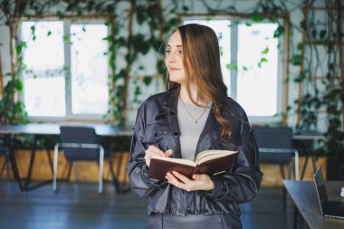 Ofisteki genç bir kadın not defterine not alıyor. Bir iş kadını modern bir çalışma alanında çalışır.