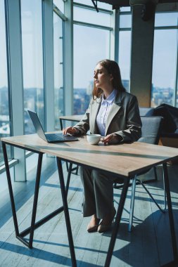 Genç bir kadın masada dizüstü bilgisayarla çalışıyor. Dizüstü bilgisayarla projede çalışan düşünceli bir kadın.