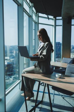 Genç bir kadın masada dizüstü bilgisayarla çalışıyor. Dizüstü bilgisayarla projede çalışan düşünceli bir kadın.