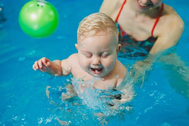 Bebekler için yüzme havuzu. 8 aylık küçük bir çocuk bir koçla havuzda yüzmeyi öğreniyor..
