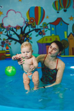 Bebekler için yüzme havuzu. 8 aylık küçük bir çocuk bir koçla havuzda yüzmeyi öğreniyor..