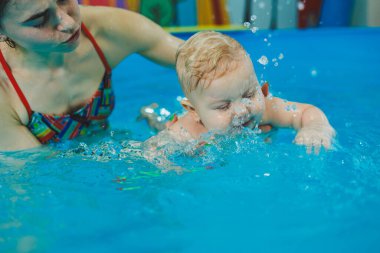 Bebekler için yüzme havuzu. 8 aylık küçük bir çocuk bir koçla havuzda yüzmeyi öğreniyor..