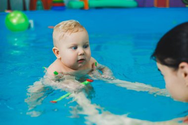 Bebekler için yüzme havuzu. 8 aylık küçük bir çocuk bir koçla havuzda yüzmeyi öğreniyor..