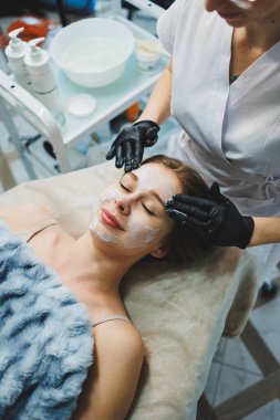 Tıp ve kozmetoloji. Siyah eldivenli bir güzellik uzmanının elleri yüze masaj yapıyor. Kişisel cilt bakımı. Yüze nemlendirici soyulan maske.