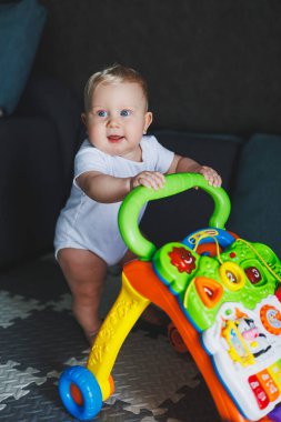 Mavi gözlü bir bebek yürüteç yardımıyla yürümeyi öğrenir. Bebek gelişiyor ve ayakta durmayı öğreniyor.