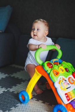 Mavi gözlü bir bebek yürüteç yardımıyla yürümeyi öğrenir. Bebek gelişiyor ve ayakta durmayı öğreniyor.