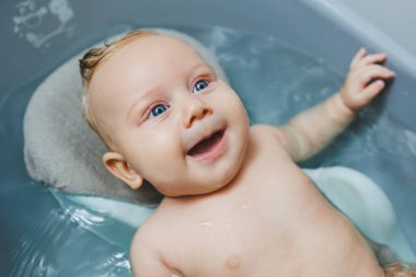 Küçük mavi gözlü bir bebek bir banyoda banyo yapıyor. Bir bebek banyo yapıyor ve gülümsüyor..