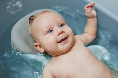 Küçük mavi gözlü bir bebek bir banyoda banyo yapıyor. Bir bebek banyo yapıyor ve gülümsüyor..