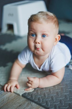Beyaz tulumlu küçük bir çocuk temiz ve sıcak zeminde sürünmeyi öğreniyor. Sevimli mavi gözlü bir bebeğin ev fotoğrafı..