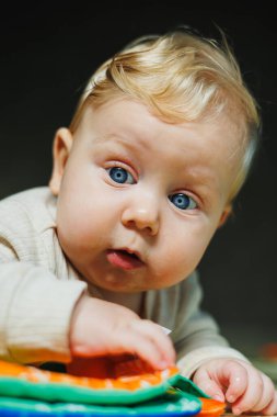 Beyaz tulumlu küçük bir çocuk temiz ve sıcak zeminde sürünmeyi öğreniyor. Sevimli mavi gözlü bir bebeğin ev fotoğrafı..
