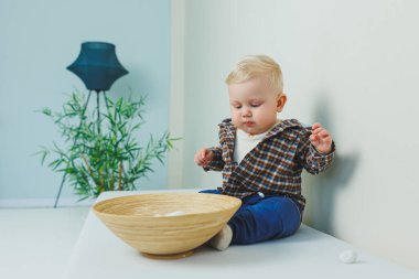 9 aylık şık gömlekli, pantalonlu ve spor ayakkabılı bir erkek bebek bir desteğin yanında duruyor..