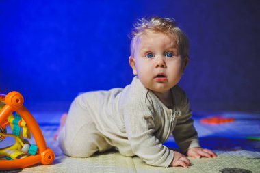 Sevimli sarışın bebek evde bebek oyuncaklarıyla oynuyor halının üzerinde oturuyor. Gülümseyen küçük bir çocuk oyuncak kullanıyor, ip çiğniyor. Çocuk gelişimi